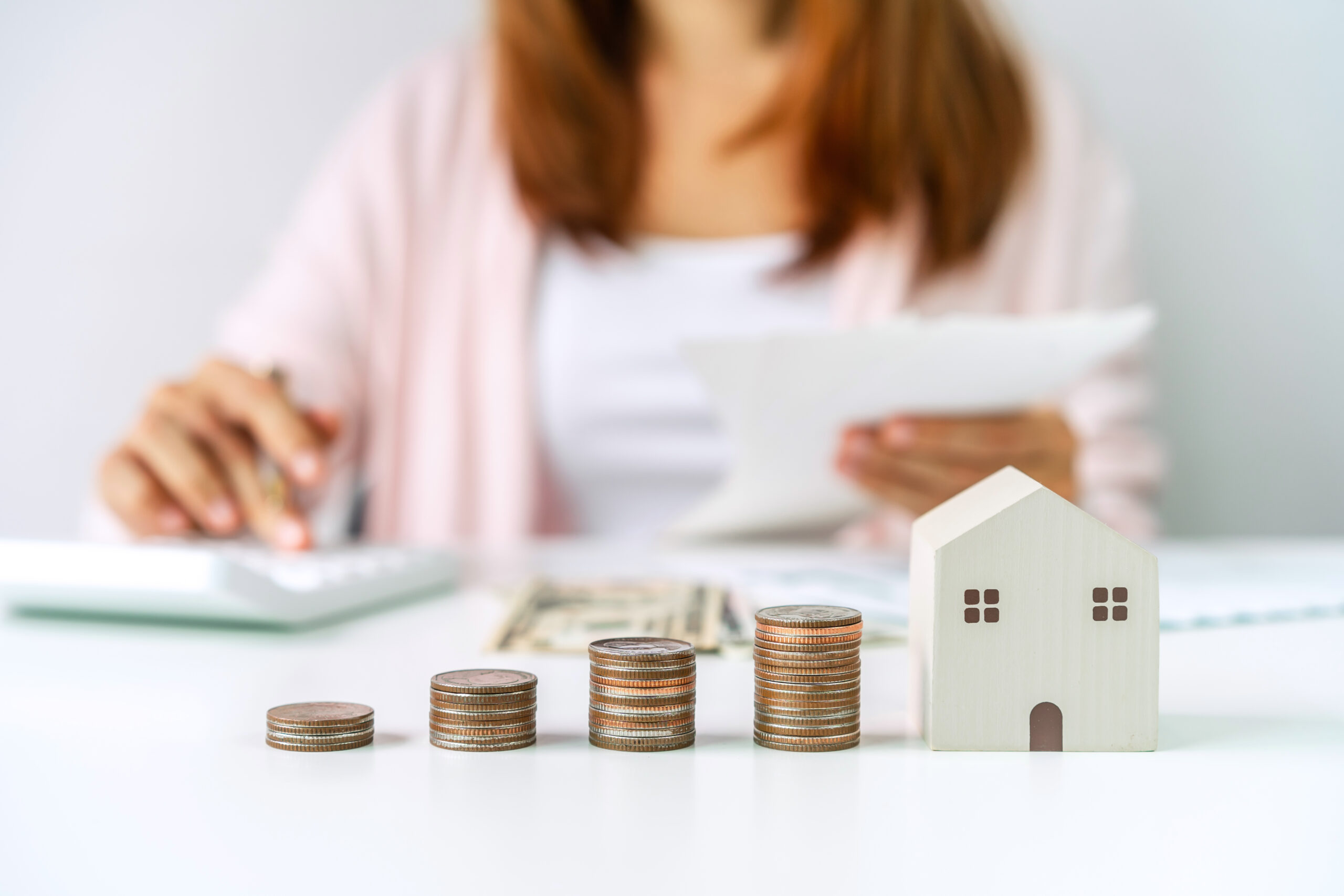 Young woman calculating home expenses with stack of coins, Saving money for property investment concept