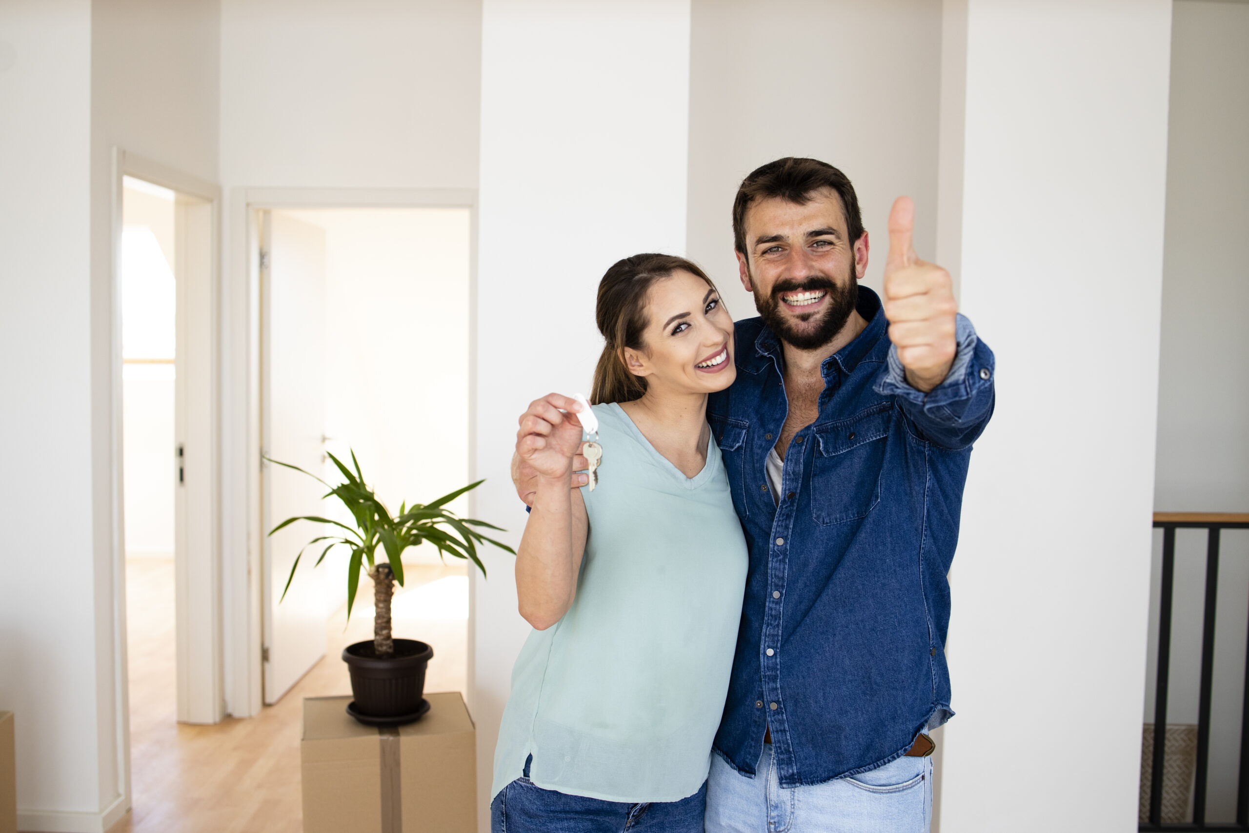 Portrait of smiling caucasian couple holding thumbs up and key of their new apartment real estate.
