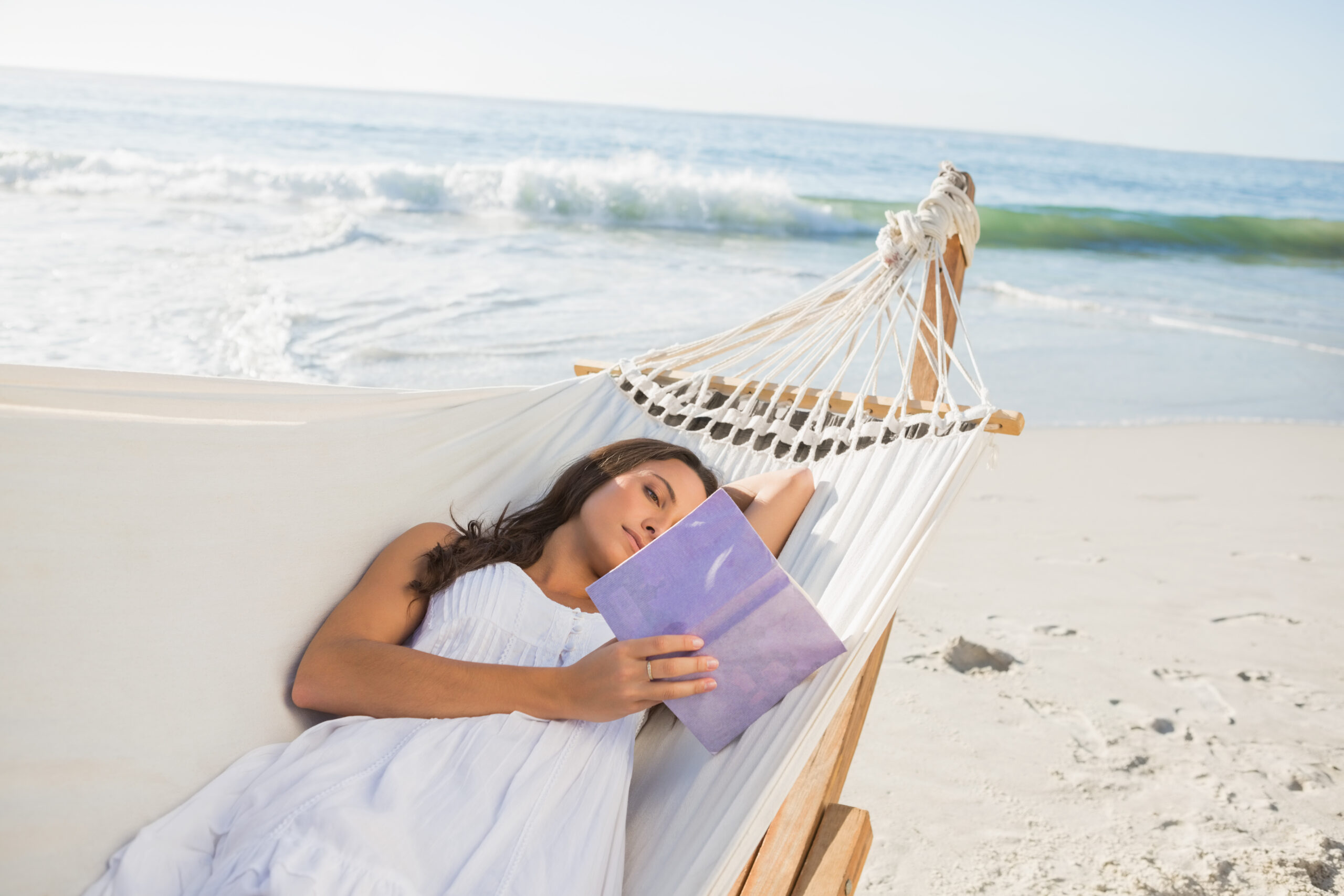 Woman lying on hammock reading book on the beach