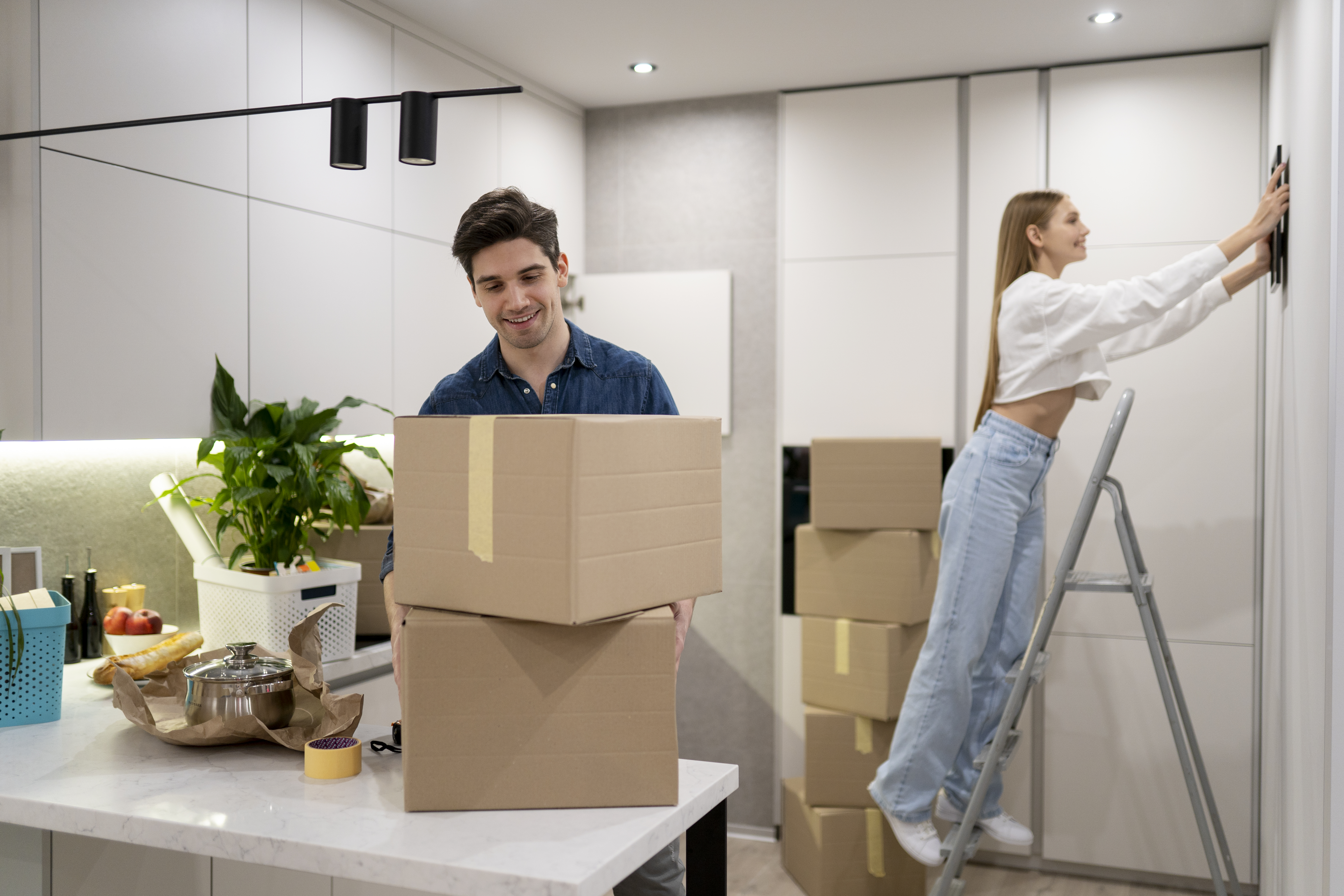 woman-hanging-frame-wall-while-her-boyfriend-is-handling-boxes