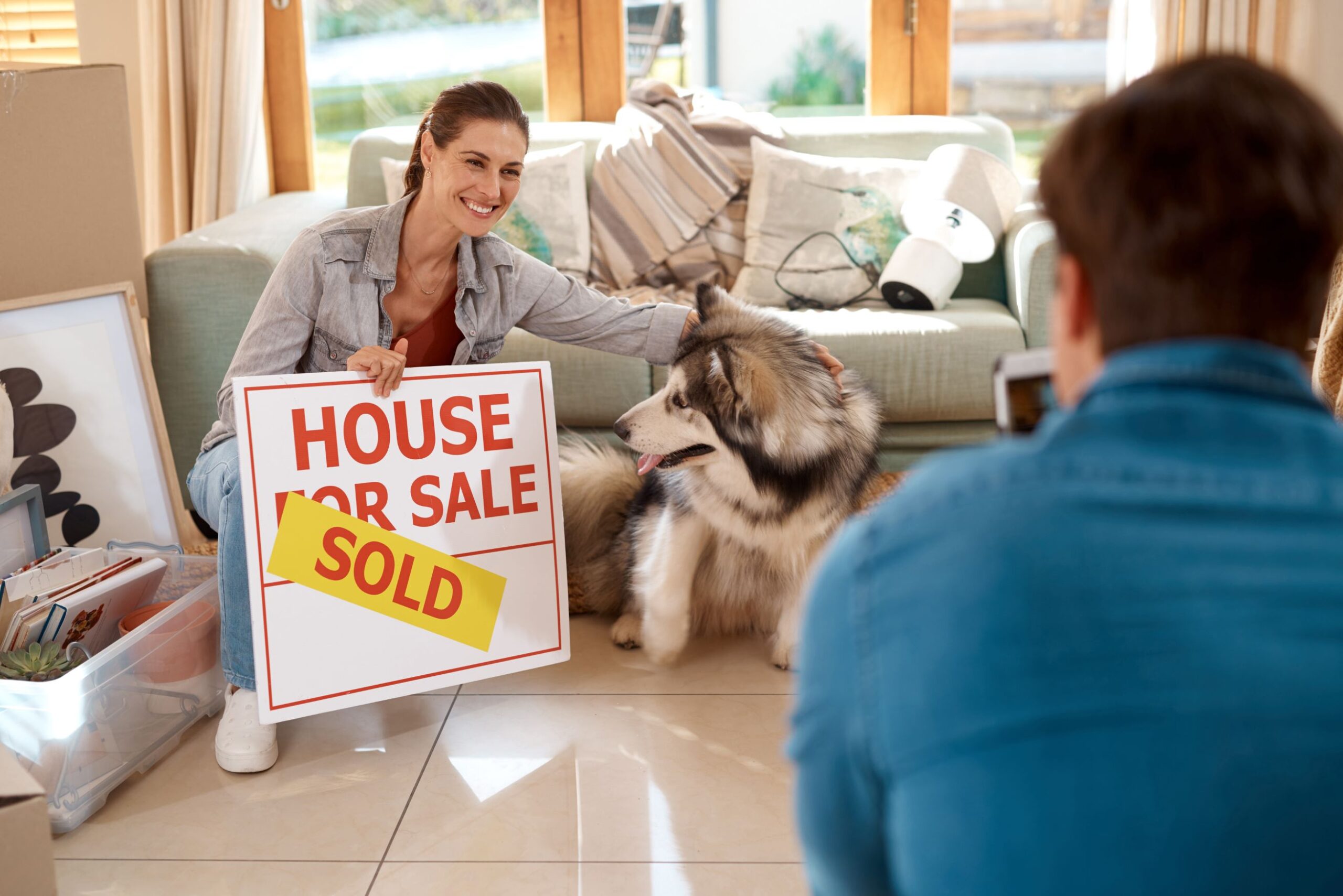 house-sold-woman-unpacking-living-room-with-pet-happiness-man-taking-picture-new-homeowners-dog-smile-smartphone-new-lounge-with-clutter-moving-settling-pride