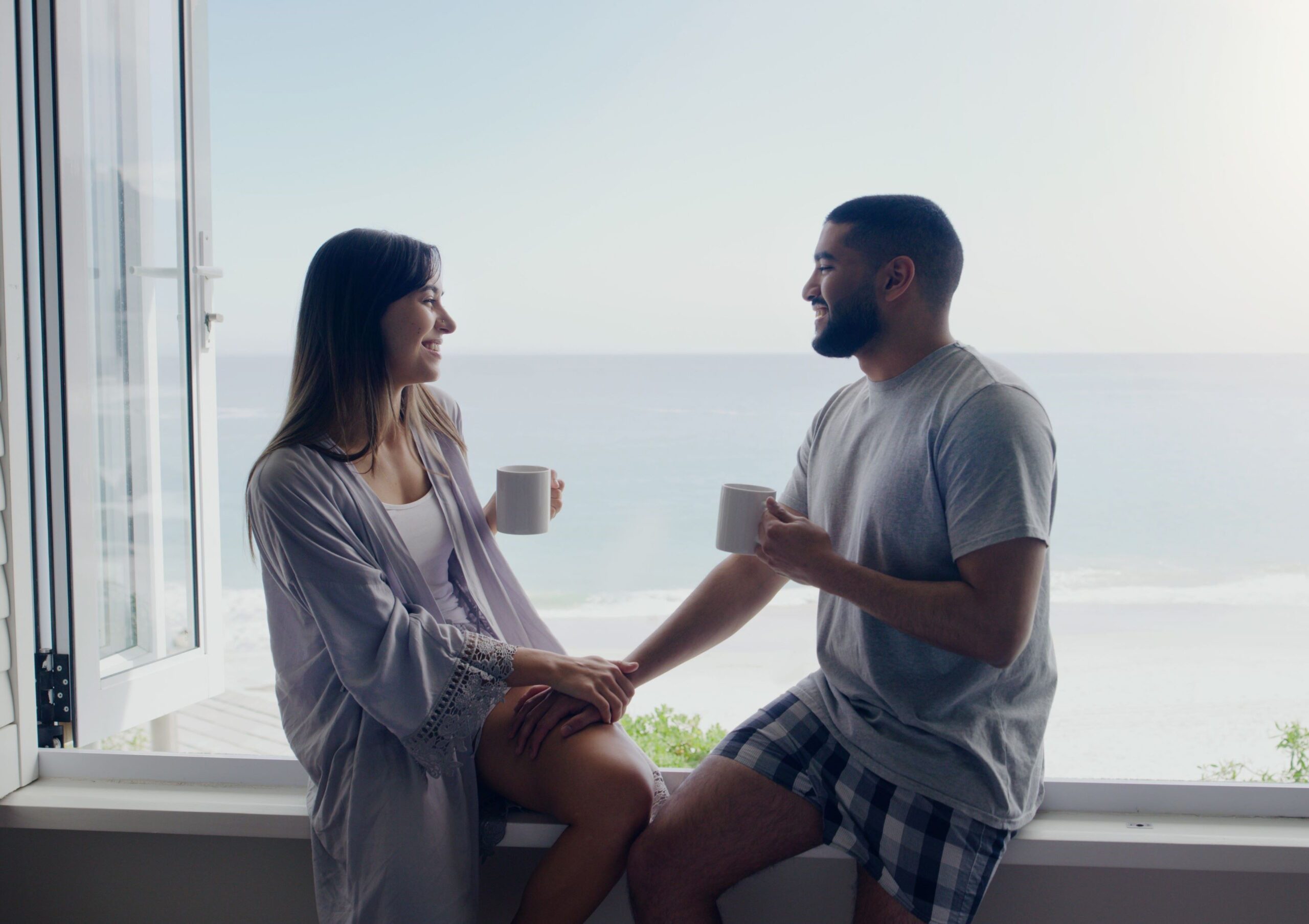 Pareja disfrutando una bebida caliente y mirando el mar desde la venta de su casa de playa