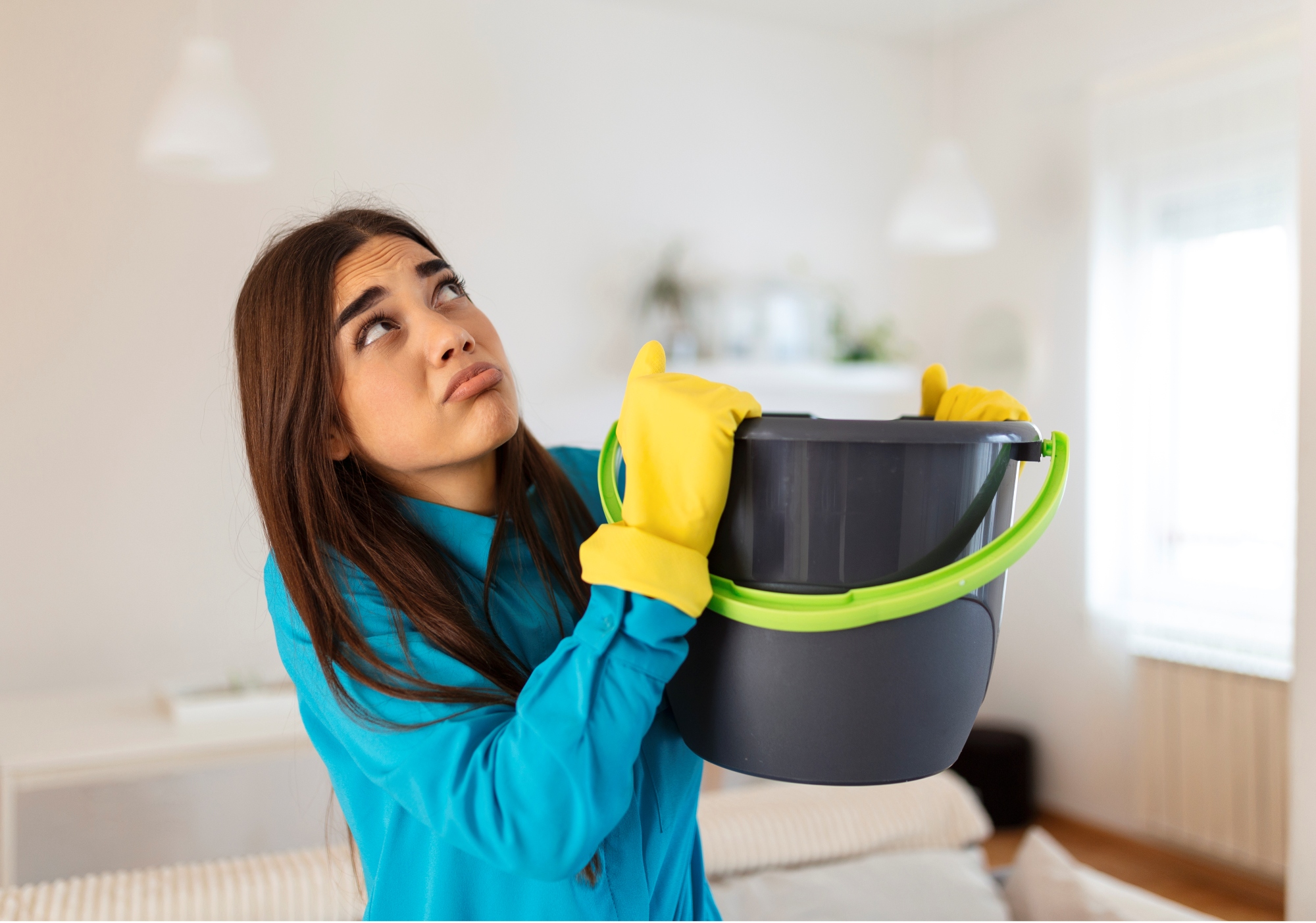 joven-mujer-sorprendida-mira-el-techo-mientras-recolecta-agua-que-se-filtra-en-la-sala-de-estar-en-casa